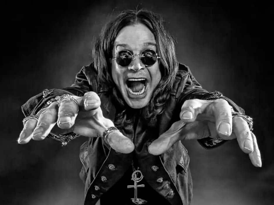 Um jovem Ozzy Osbourne, no final dos anos 60, em preto e branco, em uma encruzilhada de uma rua industrial de Birmingham. De um lado, uma fábrica sombria; do outro, um palco com uma luz brilhante. Ele está olhando para o palco com uma expressão de determinação. O estilo é de uma foto de filme granulado, dramático, alta resolução, proporção 16:9.